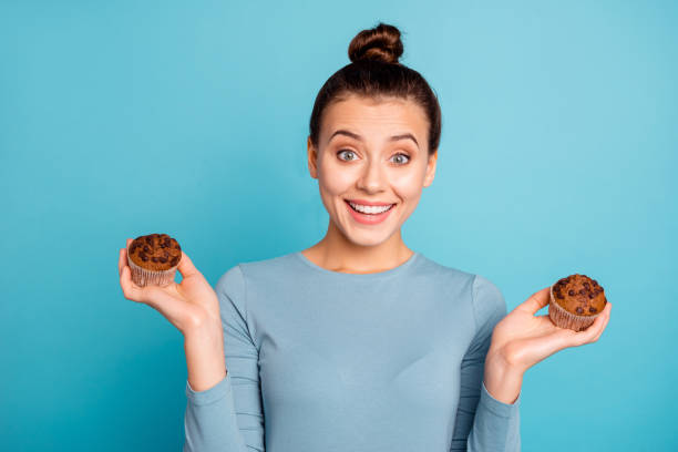 Close up photo beautiful amazing she her lady advising buy buyer try new yummy just baked tasty cacao color muffins hold hands arms wear casual sweater pullover isolated blue bright background Close up photo beautiful amazing she her lady advising buy buyer try new yummy just baked tasty cacao color muffins hold hands arms wear casual sweater pullover isolated blue bright background. topknot stock pictures, royalty-free photos & images