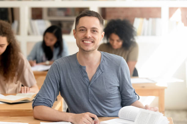 istock Smiling guy sitting at desk in classroom looking at camera 1146488505