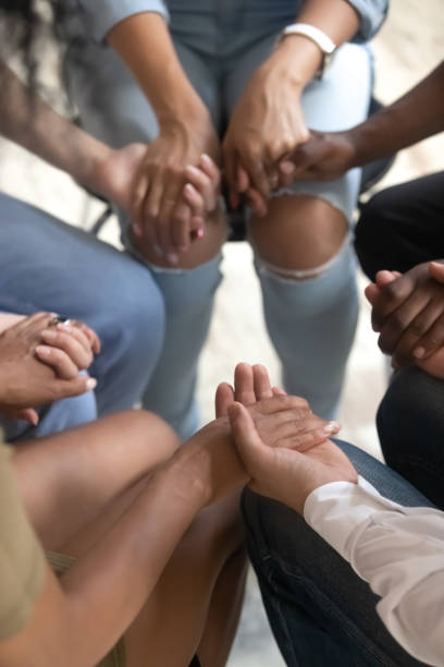 Closeup view people sitting together holding hands during therapy session Close up vertical view diverse people sitting on chairs in circle hold hands, drug alcohol addiction rehab, support group counseling, therapy session, religious team, psychological help trust concept alcoholics anonymous photos stock pictures, royalty-free photos & images