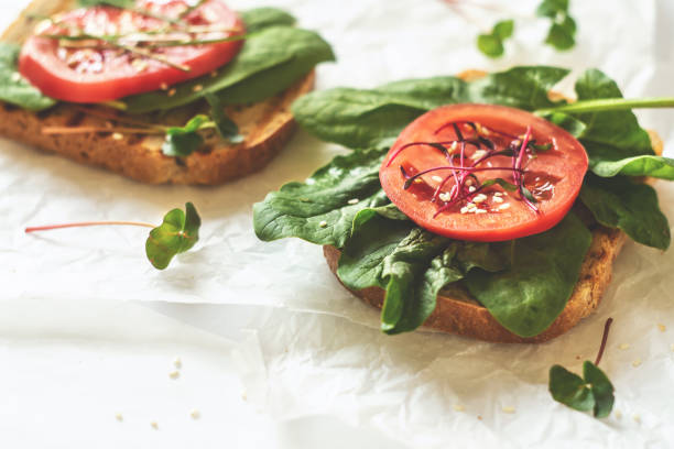 close up of a cheese sandwich with basil and tomatoes on a white plate