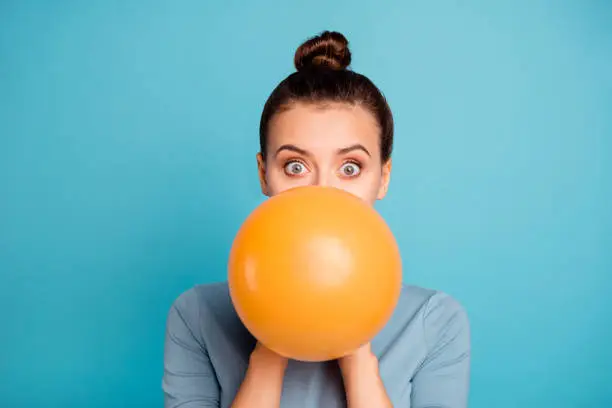 Close up photo of astonished funky teen teenager impressed omg wow unbelievable unexpected incredible wonder hide orange ballon hold hand wear modern pretty clothing isolated on blue background.