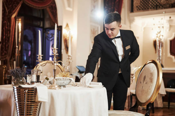 istock Front view. Process of preparing place for special visitors. Waiter in classical wear works on the servering 1146491491