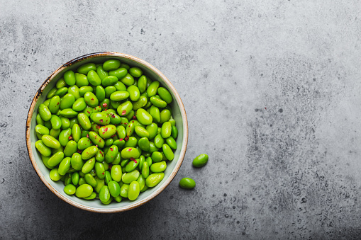 Fresh ripe green edamame beans without pods in bowl on gray stone background with space for text. Top view, close up. Light and healthy asian snack good source of protein for diet and nutrition