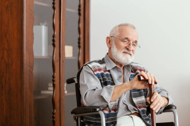 istock Elderly man sitting on a wheelchair and supporting himself with cane 1146499559