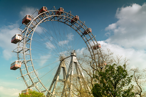 Close up of London Eye (Millennium Wheel), of the passenger capsules on the ferris wheel rotating into the white clouds and blue sky