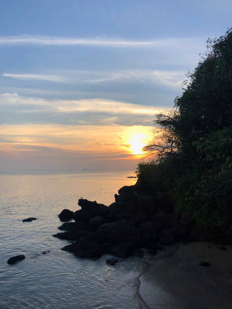 immagine della splendida spiaggia indiana di goa con cielo al tramonto rosa arancione, mare, nuvole e riflessi della costa dell'alba / tramonto nella foto della spiaggia di dona paula, goa, india meridionale, con sagome di rocce, sabbia, increspature che l - sunset vacations orange glowing foto e immagini stock