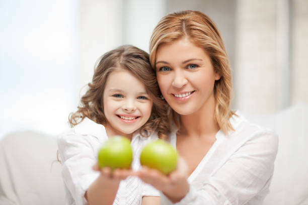 Attractive young pregnant woman holding her baby daughter under a beautiful apple tree