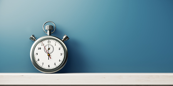 Silver colored stopwatch in front of blue wall. Horizontal composition with copy space.