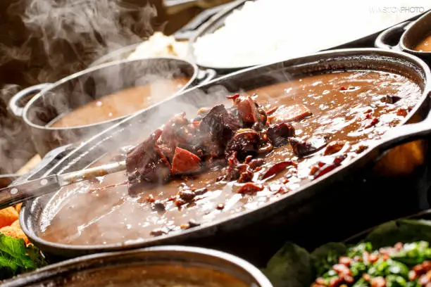 Feijoada on wooden background. Beans, Brazilian food, caipirinha, rice, farofa, orange, sun meat, cured meat, feijoada meat, bacon, pork, cabbage.