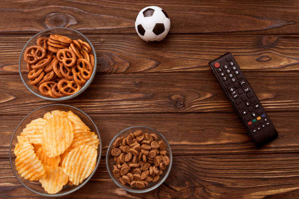 Chips, crackers, snacks, TV remote control, soccer ball on wooden table background. Chips, crackers, snacks, TV remote control, soccer ball on wooden table background. football match, fans. sport. remote control on table stock pictures, royalty-free photos & images