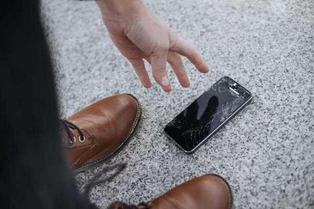 istock Young woman picks up her Broken smartphone with cracked screen glass after falling 1146525201