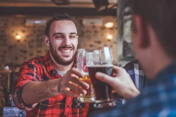 Hipster friends clinking with beer mugs in pub