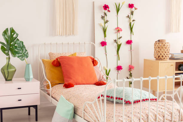 White single metal bed with colorful pillows and doted bedding in chic boho bedroom interior