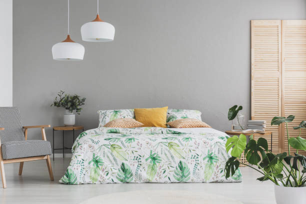 istock Double bed with botanical accents on sheets and peach colored pillows in grey scandinavian bedroom, copy space on the empty grey wall 1146544589