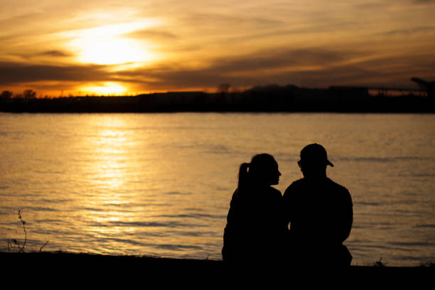Silhouette of lovers enjoying sunset on the banks of a river. stock photo