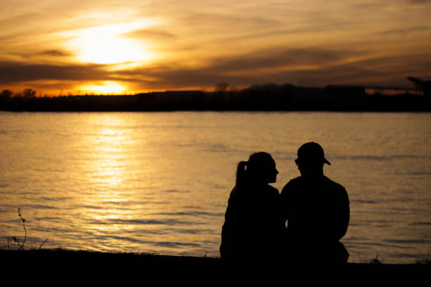 silhouette of lovers enjoying sunset on the banks of a river. - date night imagens e fotografias de stock