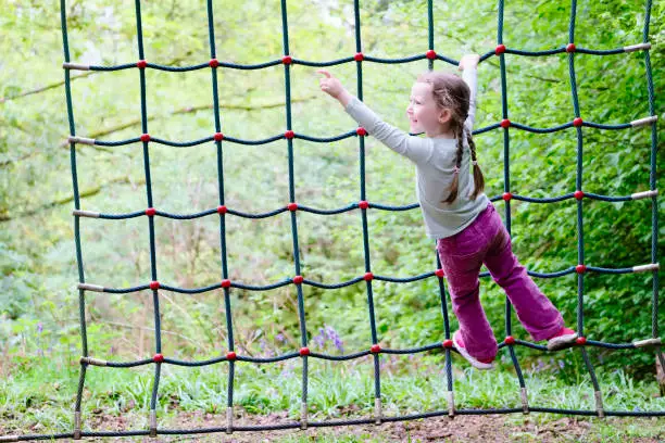 Young girl climbing on rope net frame in outdoor woodland adventure parkground uk