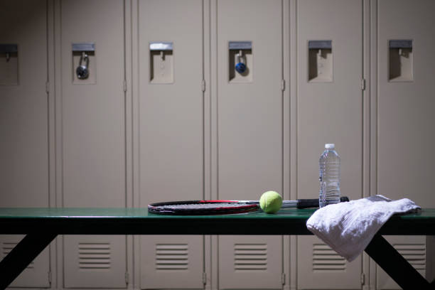 Tennis sports equipment in school gymnasium locker room. Various sports equipment on bench inside high school or college gymnasium locker room. Items include: tennis racket, tennis ball, water, towel. tennis ball container stock pictures, royalty-free photos & images