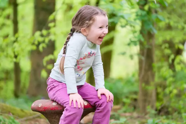 Young girl sitting laughing hands on knees in woodland forest uk