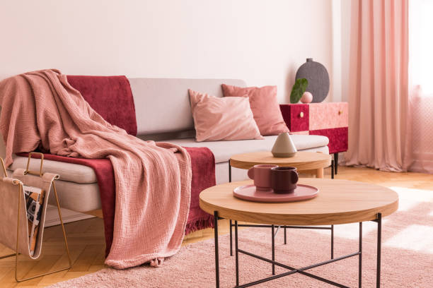 istock Two coffee cups on wooden coffee table next to classy grey settee with pastel pink pillows and burgundy and pastel pink blankets in chic living room 1146546601
