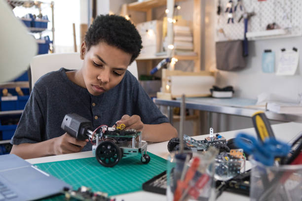 Teen boy solders wires to build robot A serious teen boy uses a soldering gun to connect wires as he builds a robot at home. stem topic stock pictures, royalty-free photos & images