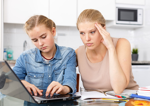 Strict woman supervising study of her teenage daughter in kitchen