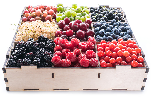 Colorful berries in wooden box on white background. Close-up.