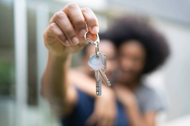 Young couple in front of a house, holding keys of their new home Young couple in front of a house, holding keys of their new home house key stock pictures, royalty-free photos & images