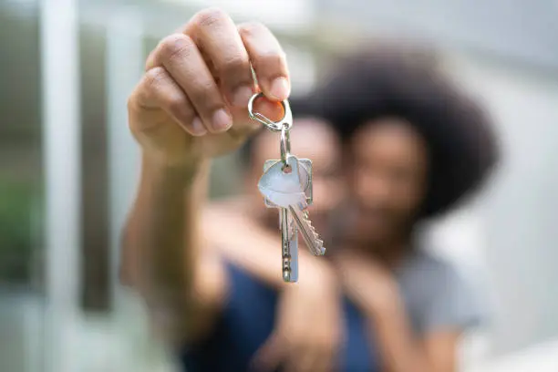 Photo of Young couple in front of a house, holding keys of their new home