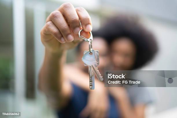 Young Couple In Front Of A House Holding Keys Of Their New Home - Fotografias de stock e mais imagens de Proprietário de Casa