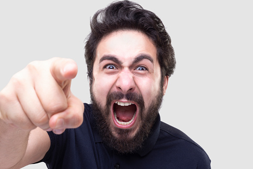 Portrait of a young man screaming with furious facial expression over gray background. Horizontal composition. Studio shot.