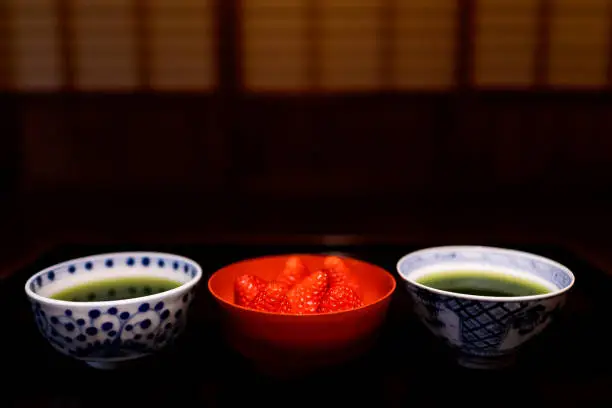 Traditional japanese bowls cups with matcha green tea and strawberries in machiya house with black lacquered wood table and dessert dish