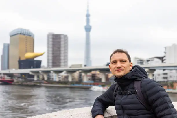 Tokyo, Japan Sumida district area cityscape skyline with young tourist man leaning on railing of bridge by river in downtown on cloudy day