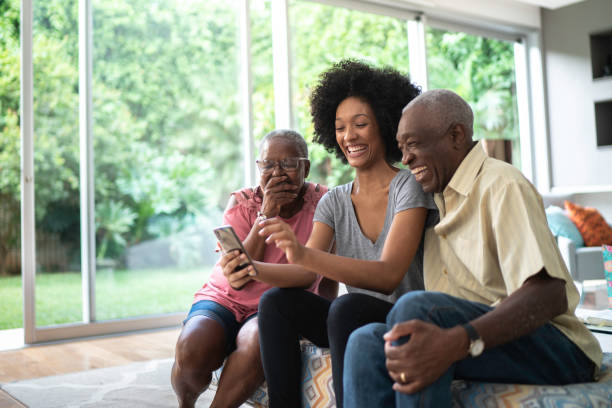 nipote afro che mostra foto nel suo cellulare ai nonni, persone che sorridono e si divertono - grandmother senior adult smiling women foto e immagini stock