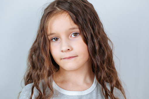 Close up of white teenage girl looking to camera smiling. Her hair is back and tied up she is wearing a white jumper and it is against a plain background.