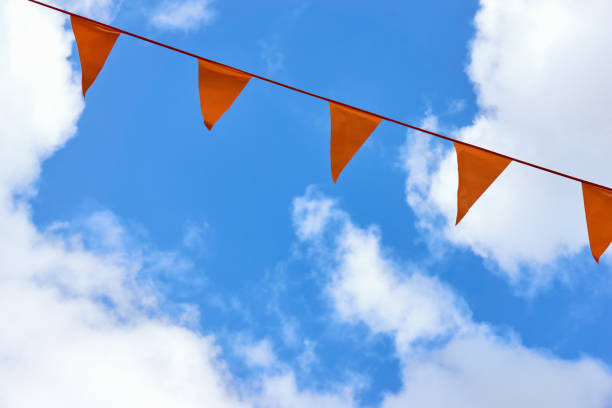A row of orange triangle pennant banner flags on Koningsdag. A national holiday in the Netherlands against a blue sky with clouds and copy space