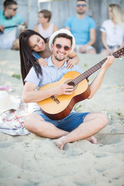 młoda, szczęśliwa i piękna para z gitarą na plaży - beach couple satisfaction playing zdjęcia i obrazy z banku zdjęć