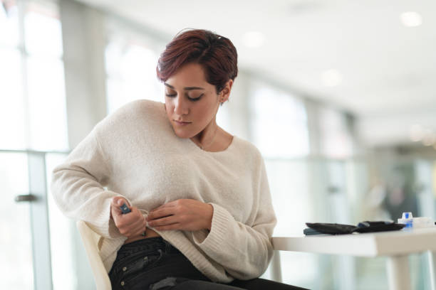 Diabetic woman uses insulin pen A woman of Middle Eastern ethnicity is seated at a table. She is taking a break from work and is in her workplace's lobby. The woman is diabetic and is using an insulin pen near her hip. insulin stock pictures, royalty-free photos & images