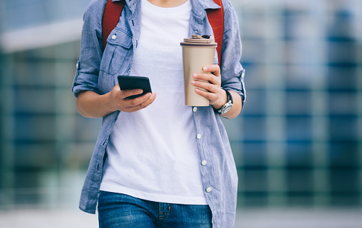 Woman commuter use mobile phone walking with coffee cup in hand