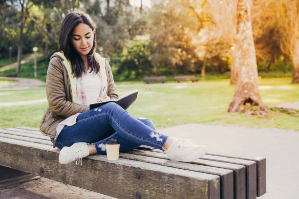 istock Pensive Asian girl making notes in diary while sitting in park 1146589838