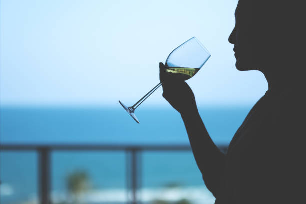 Silhouette image of a woman holding a wine glass to drink with blurred sea background