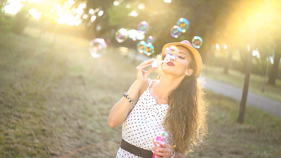 Young caucasian beautiful woman blowing bubbles in public park on a sunny day.