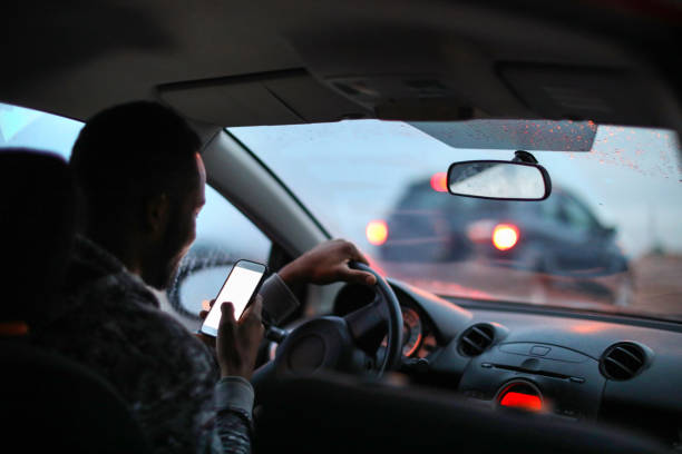 hombre africano usando su teléfono mientras conducía bajo la lluvia. - hora punta temas fotos fotografías e imágenes de stock
