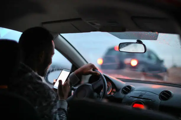 African man using his phone while driving in the rain.