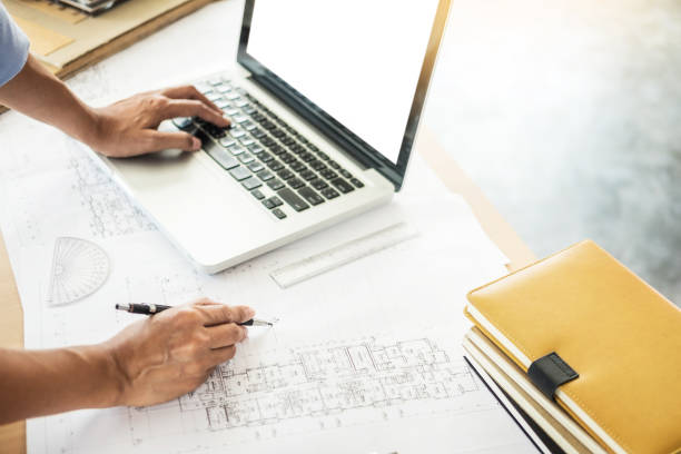 istock Cropped Hands Of Man Writing On Blueprint While Using Laptop On Desk 1146628720