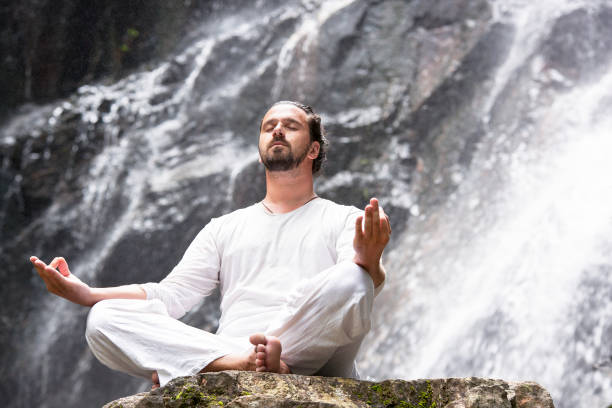 koncepcja medytacji jogi wellness. młody człowiek siedzący w pozycji lotosu na skale pod tropikalnym wodospadem. - waterfall water nature zen like zdjęcia i obrazy z banku zdjęć