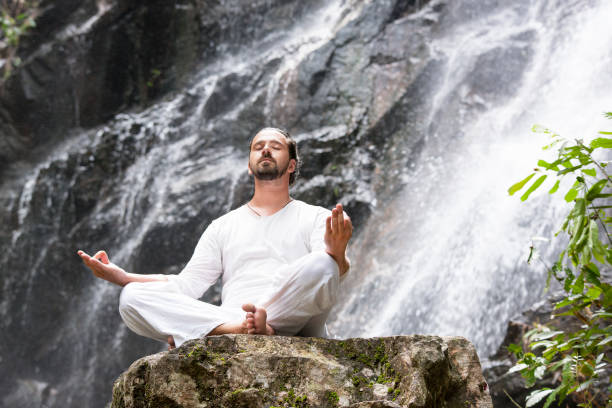 koncepcja medytacji jogi wellness. młody człowiek siedzący w pozycji lotosu na skale pod tropikalnym wodospadem. - waterfall water nature zen like zdjęcia i obrazy z banku zdjęć