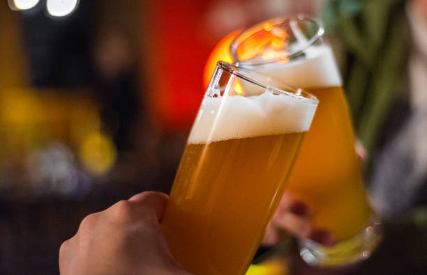 Close-up view of a two glass of beer in hand. Beer glasses clinking in bar or pub Close-up view of a two glass of beer in hand. Beer glasses clinking in bar or pub india pale ale photos stock pictures, royalty-free photos & images