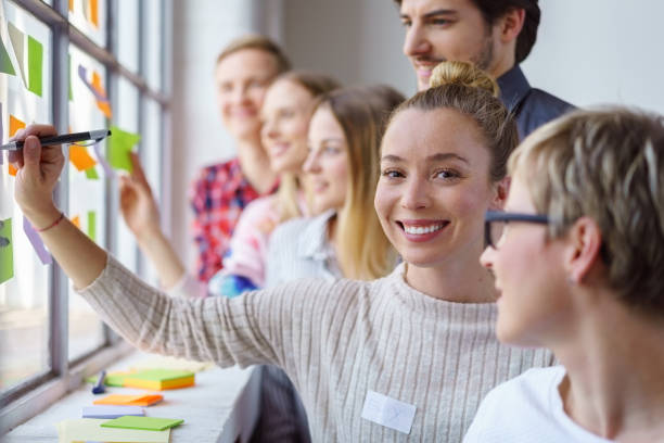 Happy office team brain storming with sticky notes A team of happy, smiling work colleagues building ideas and brain storming with sticky notes on an office window. storming stock pictures, royalty-free photos & images