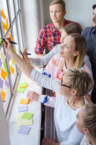 Happy, laughing work colleagues sharing ideas on sticky notes during a meeting in a brightly lit office.